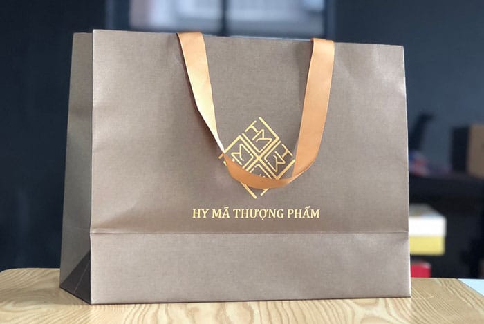 Túi giấy mỹ thuật cao cấp cho mỹ phẩm – ép kim, thúc nổi logo thương hiệu, quai lụa sang trọng, phù hợp làm quà tặng.